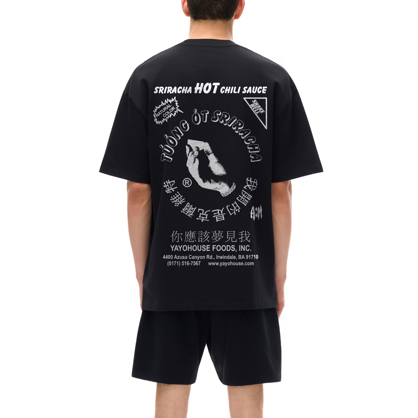 A person wearing a black Sriracha T-shirt and black shorts from behind.