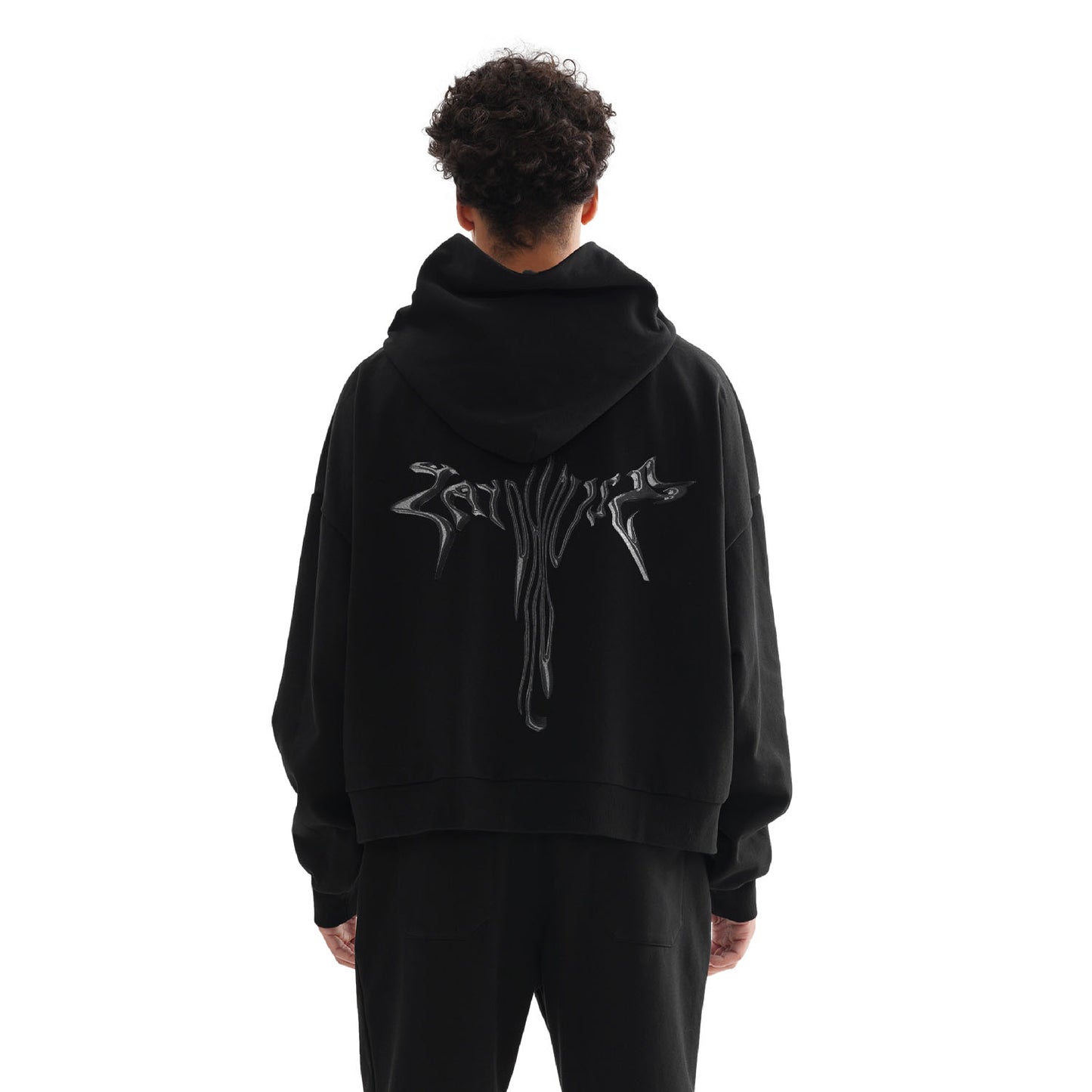 A person wearing a black hoodie and pants, standing with their back to the camera.
