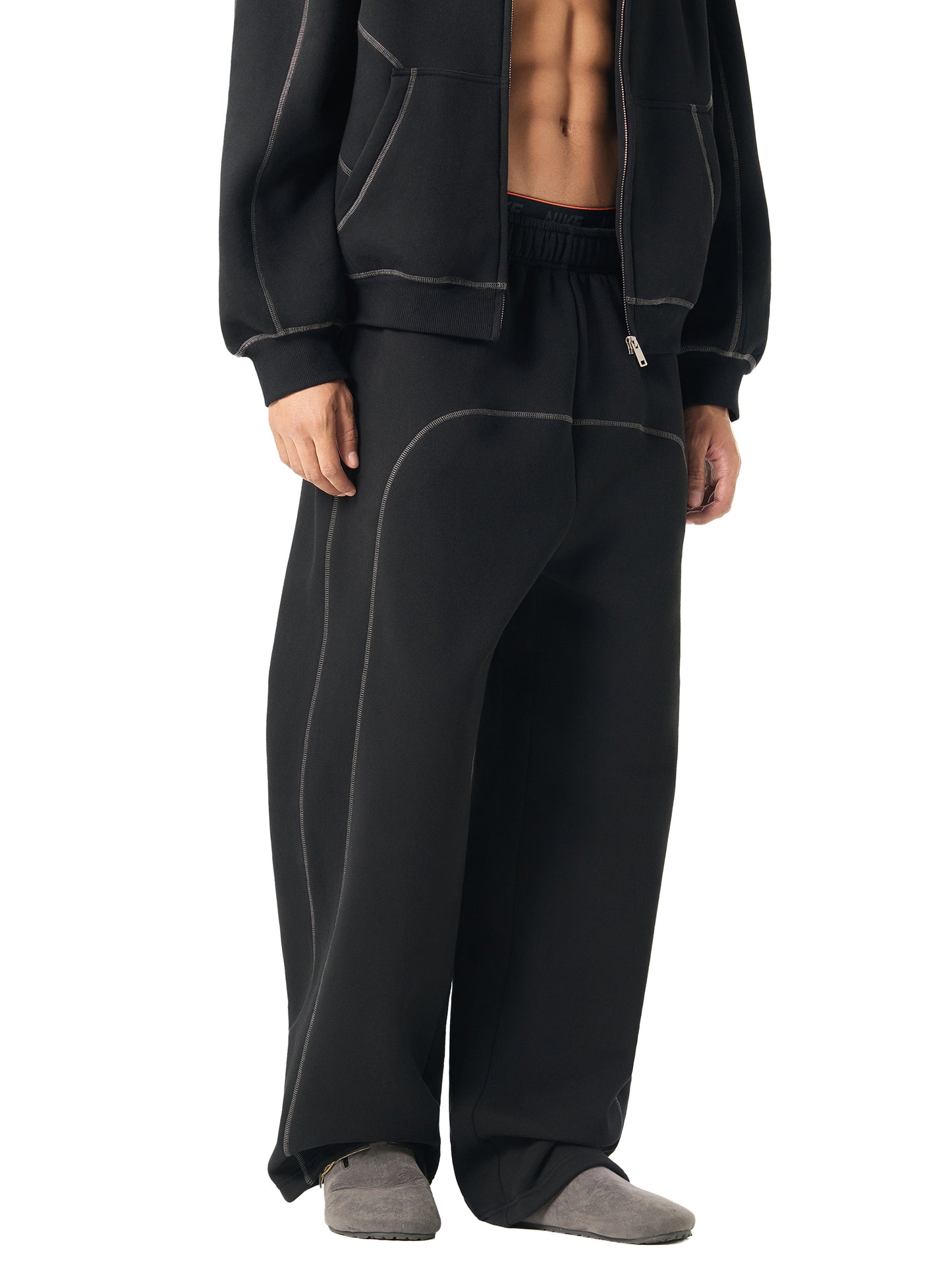 Person wearing black tracksuit pants and jacket on a white background