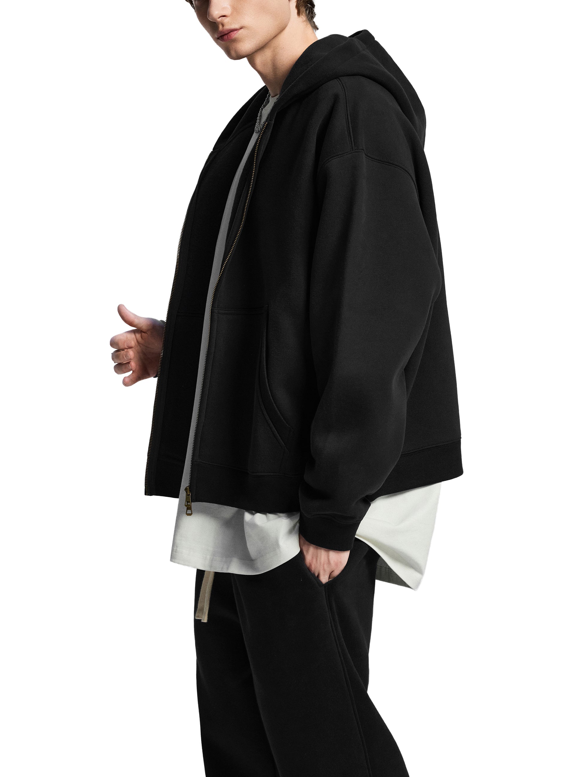 Person wearing a black hoodie over a white shirt with black pants on a white background