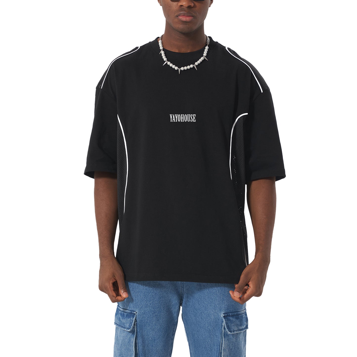 Man wearing a black "YAYOHOUSE" t-shirt, blue cargo jeans, and a pearl and spike necklace.