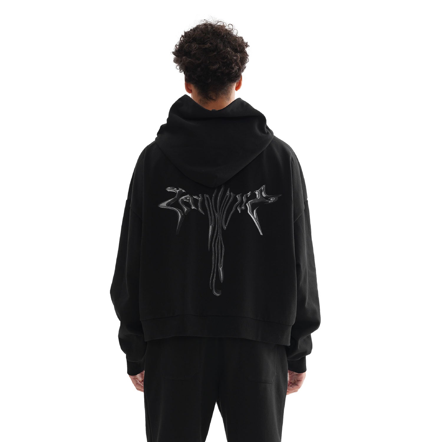 A person wearing a black hoodie and pants, standing with their back to the camera.